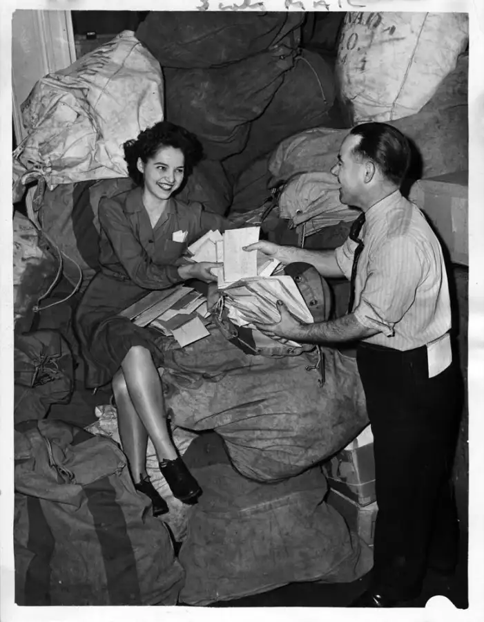 A 1945 photograph of a tax office: a woman sorting income tax forms from a mail sack while a supervisor looks on