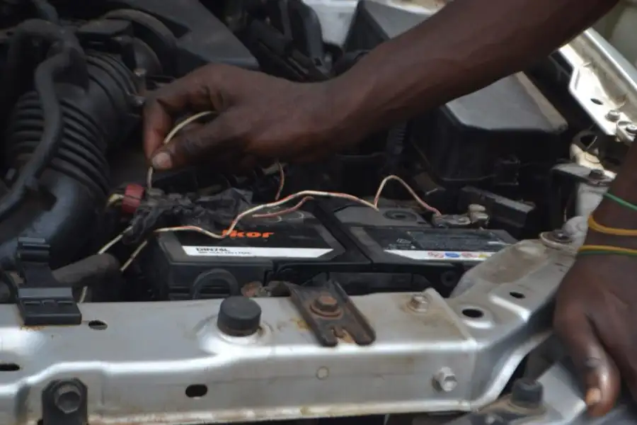 Hands connecting wires to a car battery under the hood