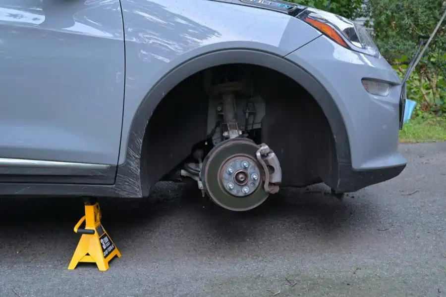 A front disc brake and caliper exposed with the wheel off, the car on a jack stand