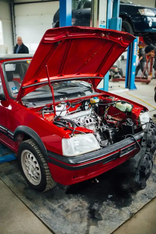 A red hatchback with its hood open inside a repair shop