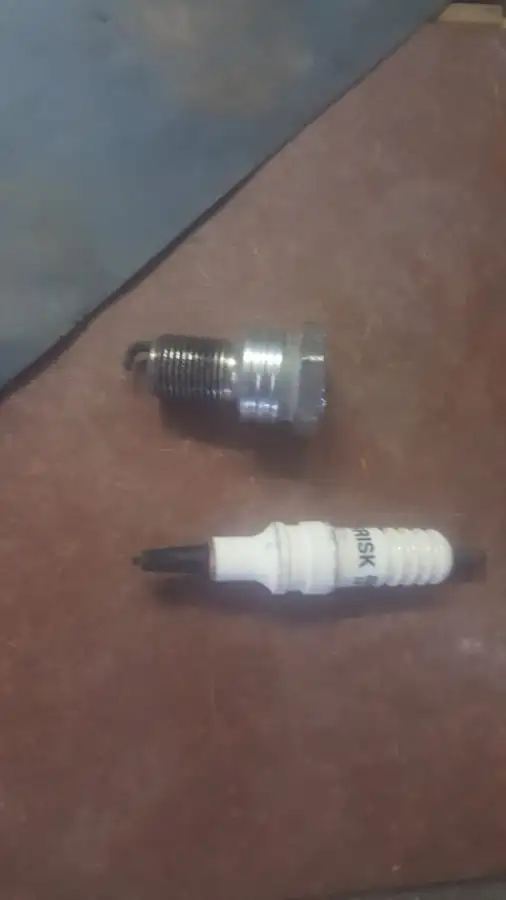 Two spark plugs lying on a brown workbench