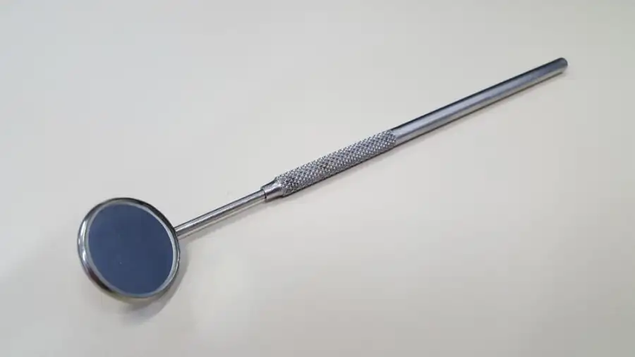 A dental mirror on a pale grey background