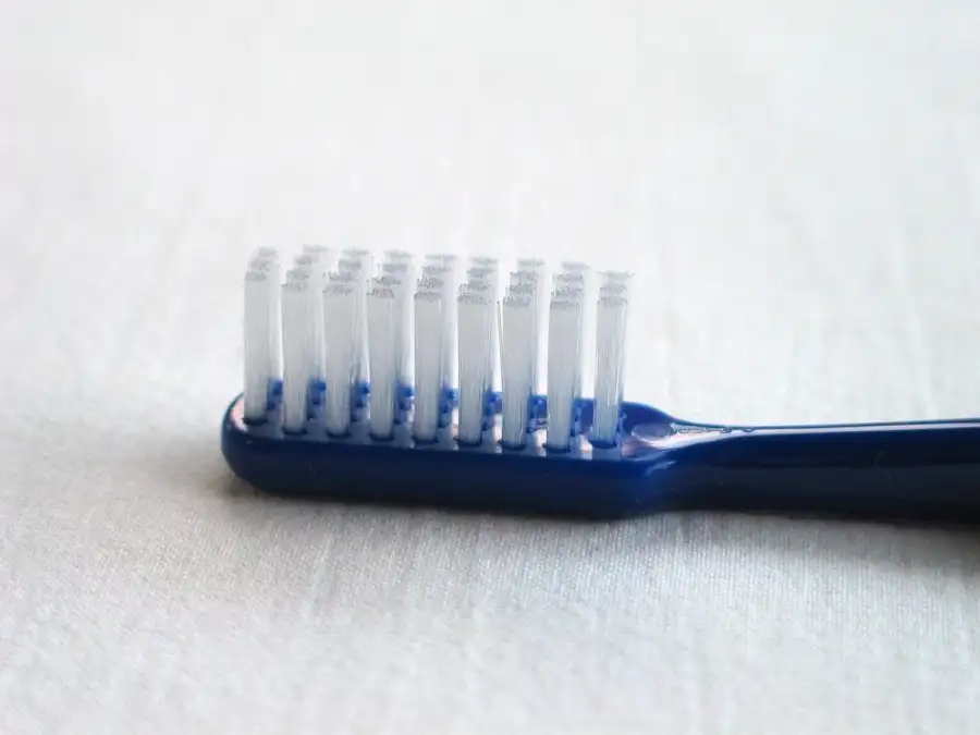 A blue toothbrush with white bristles lying on a white surface