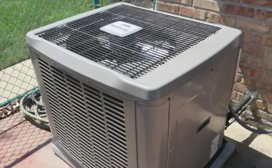 An outdoor central air conditioning condenser unit beside a brick wall