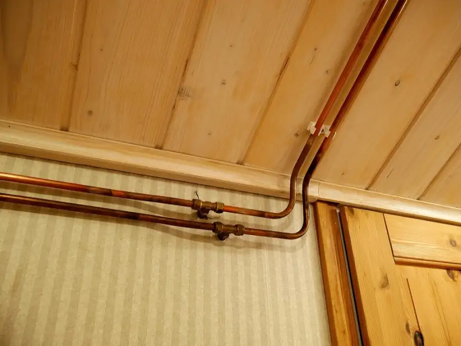 Copper water pipes running along a pine-boarded ceiling
